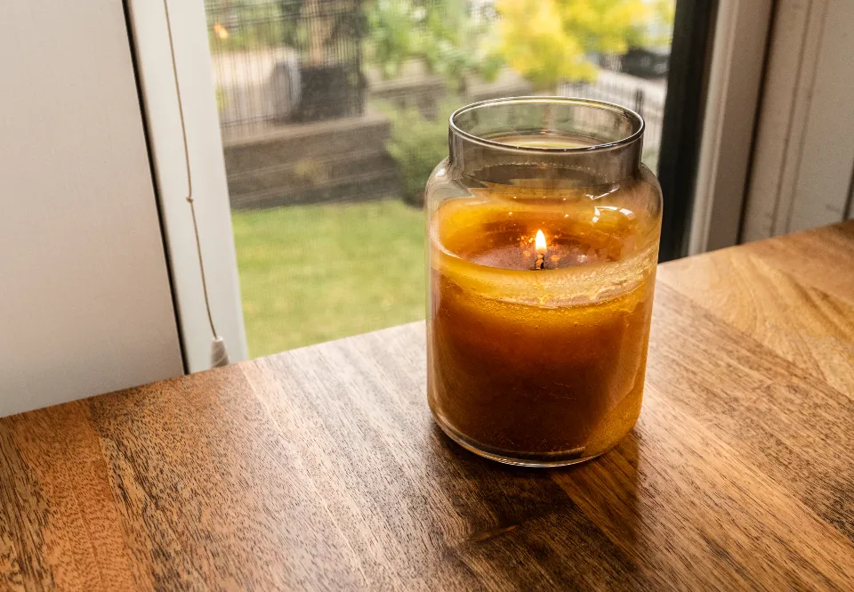 An amber candle in a clear glass jar on a wooden windowsill