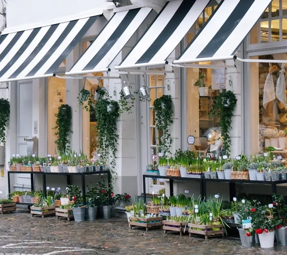 A white shop front with striped awnings, baskets and pots by the door