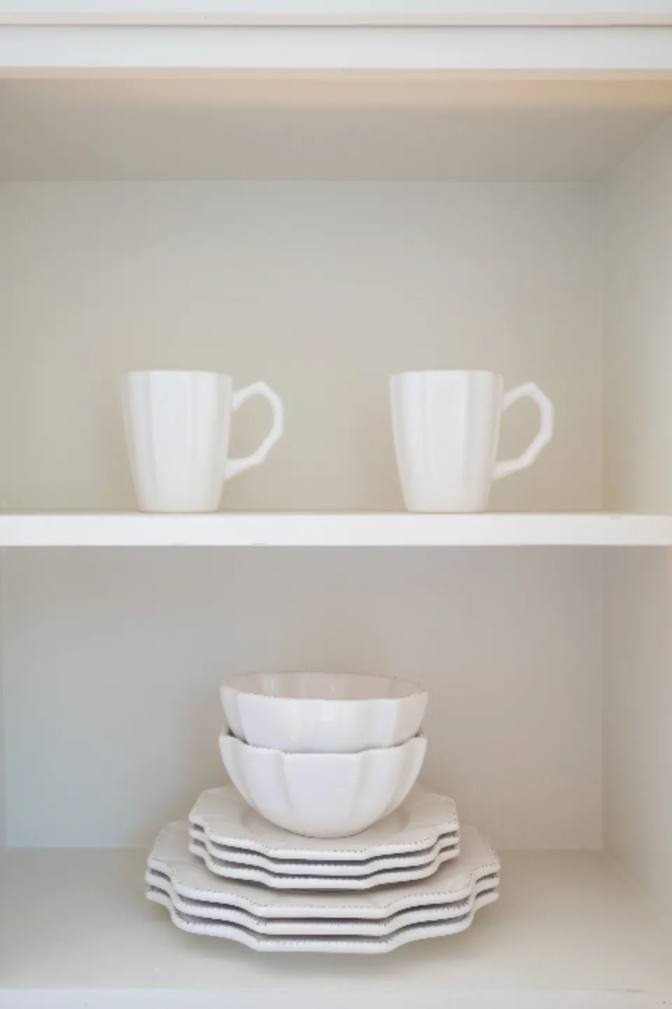 White mugs and scalloped bowls stacked on pale shelves