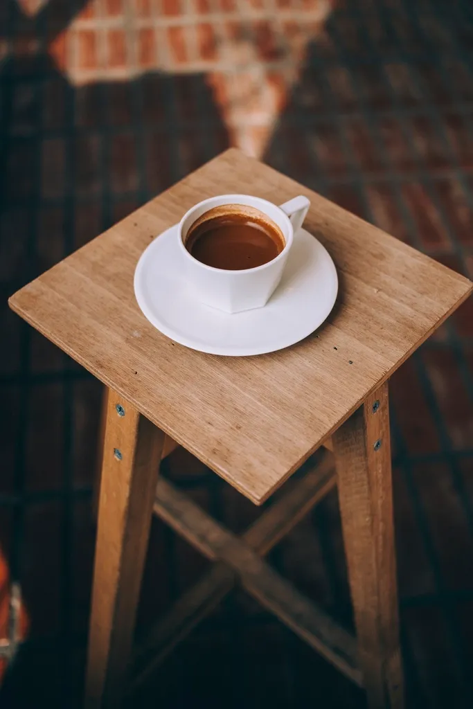 A small square wooden stool holding a white cup and saucer